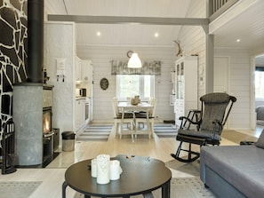 A spacious living room with a fireplace, a dining area, and a kitchen visible through an open door. - Lapinvouti by Interhome (Kittilä)
