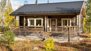 A wooden cabin with a dark roof, numbered 53, featuring a porch with wooden railings and a small bench.