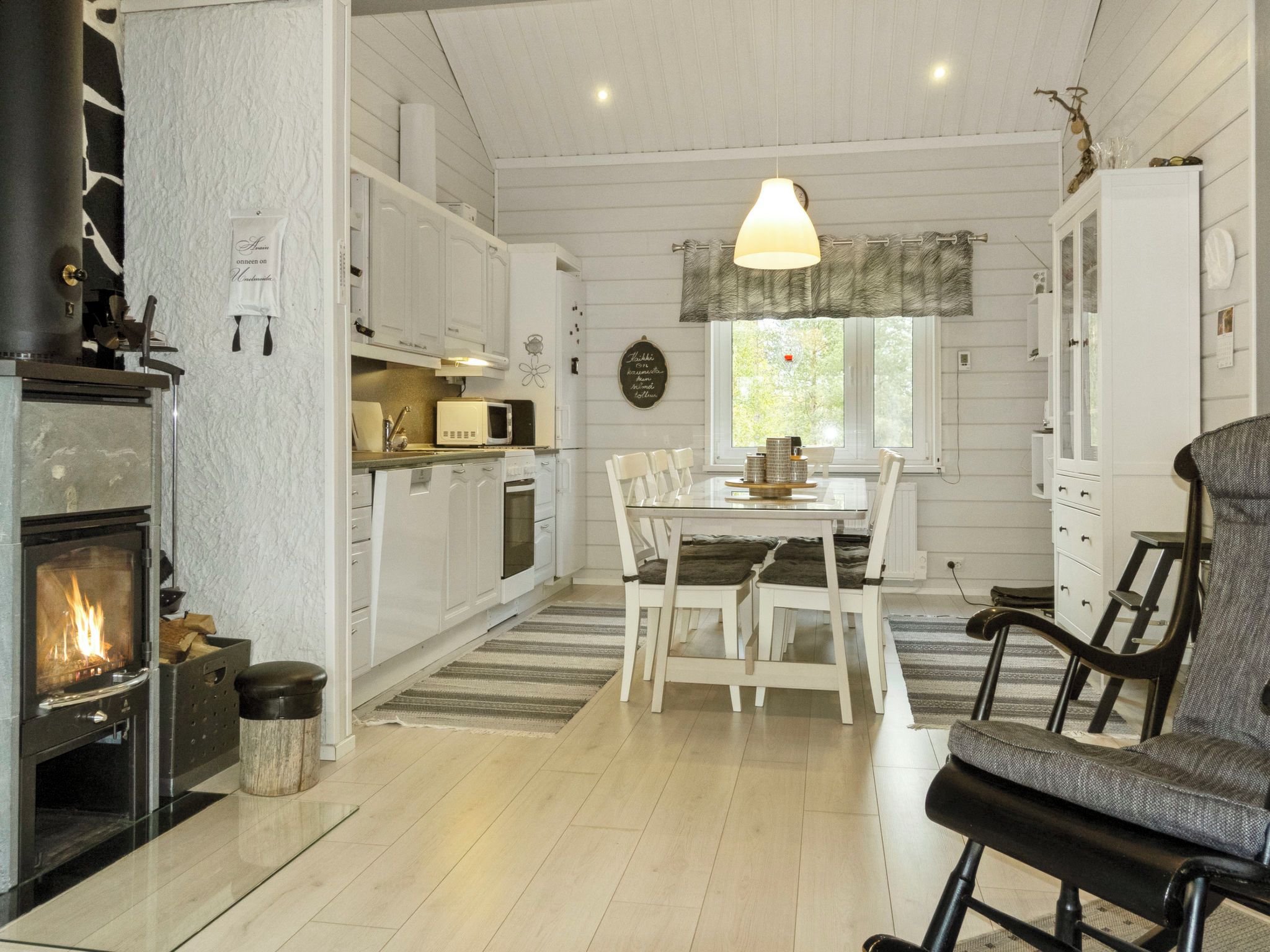A cozy kitchen with a wood-burning stove, white cabinets, and a dining area with a table and chairs.