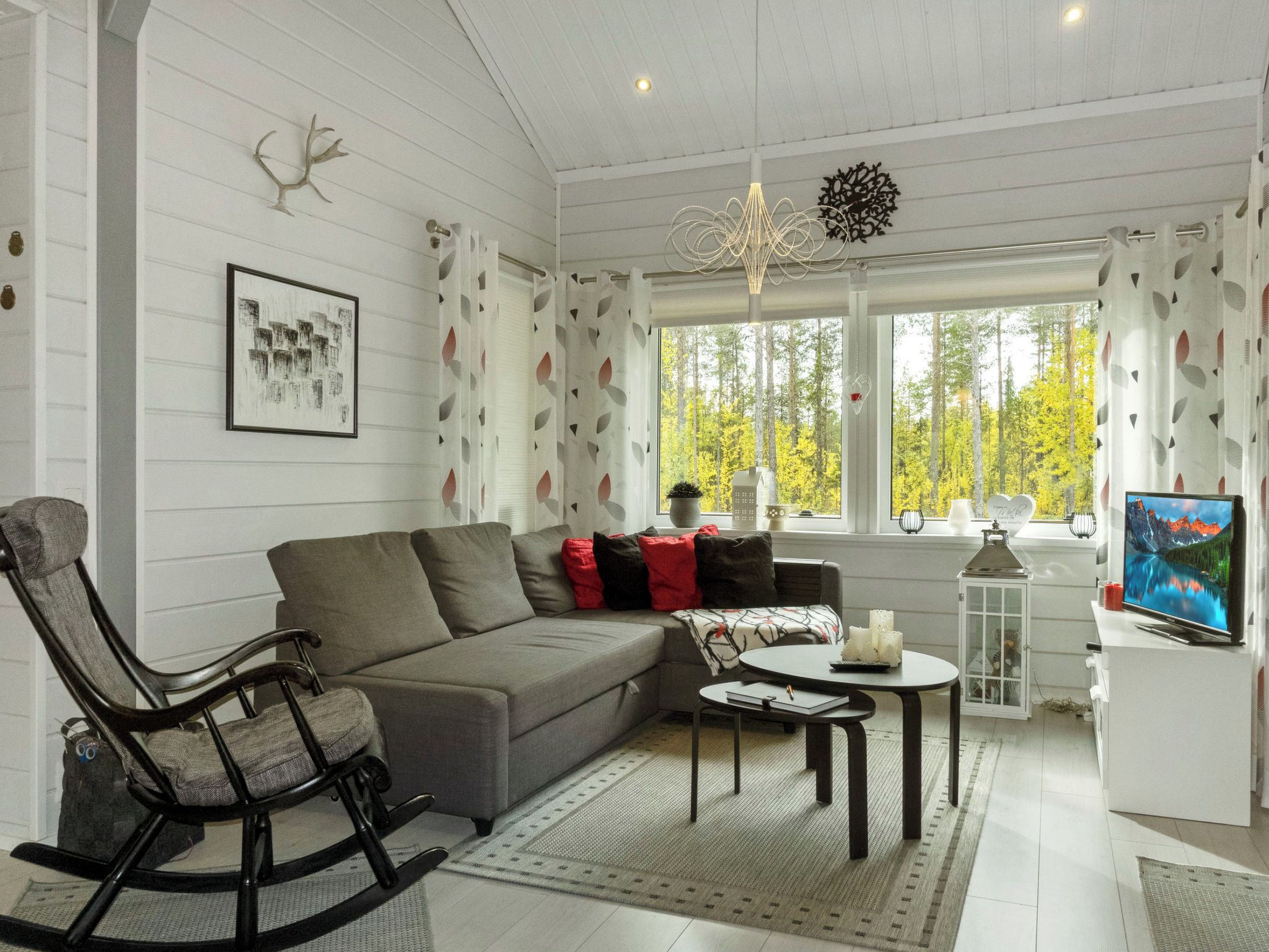 A modern living room with a grey sofa, a rocking chair, a small table, and a television.