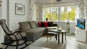 A modern living room with a grey sofa, a rocking chair, a small table, and a TV.