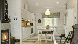A cozy kitchen with white cabinetry, a wood-burning stove, a dining table with chairs, and a hanging light fixture.