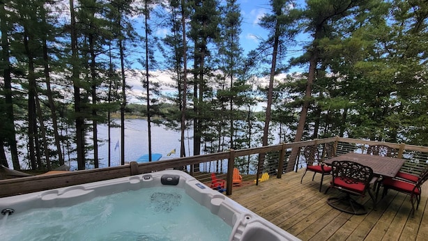 Uma banheira de hidromassagem em um deck de madeira com vista para um lago e árvores.