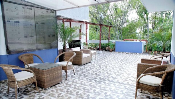A covered outdoor seating area with wicker furniture and a tiled floor. - Room-nice Boutique Guest House In South (New Delhi)