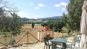 Eine Terrasse mit Tisch und Stühlen, mit Blick auf eine ländliche Landschaft aus Feldern und Hügeln.