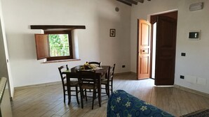Un coin repas avec une table et des chaises en bois, une fenêtre donnant sur un paysage verdoyant et une porte menant à l’extérieur.