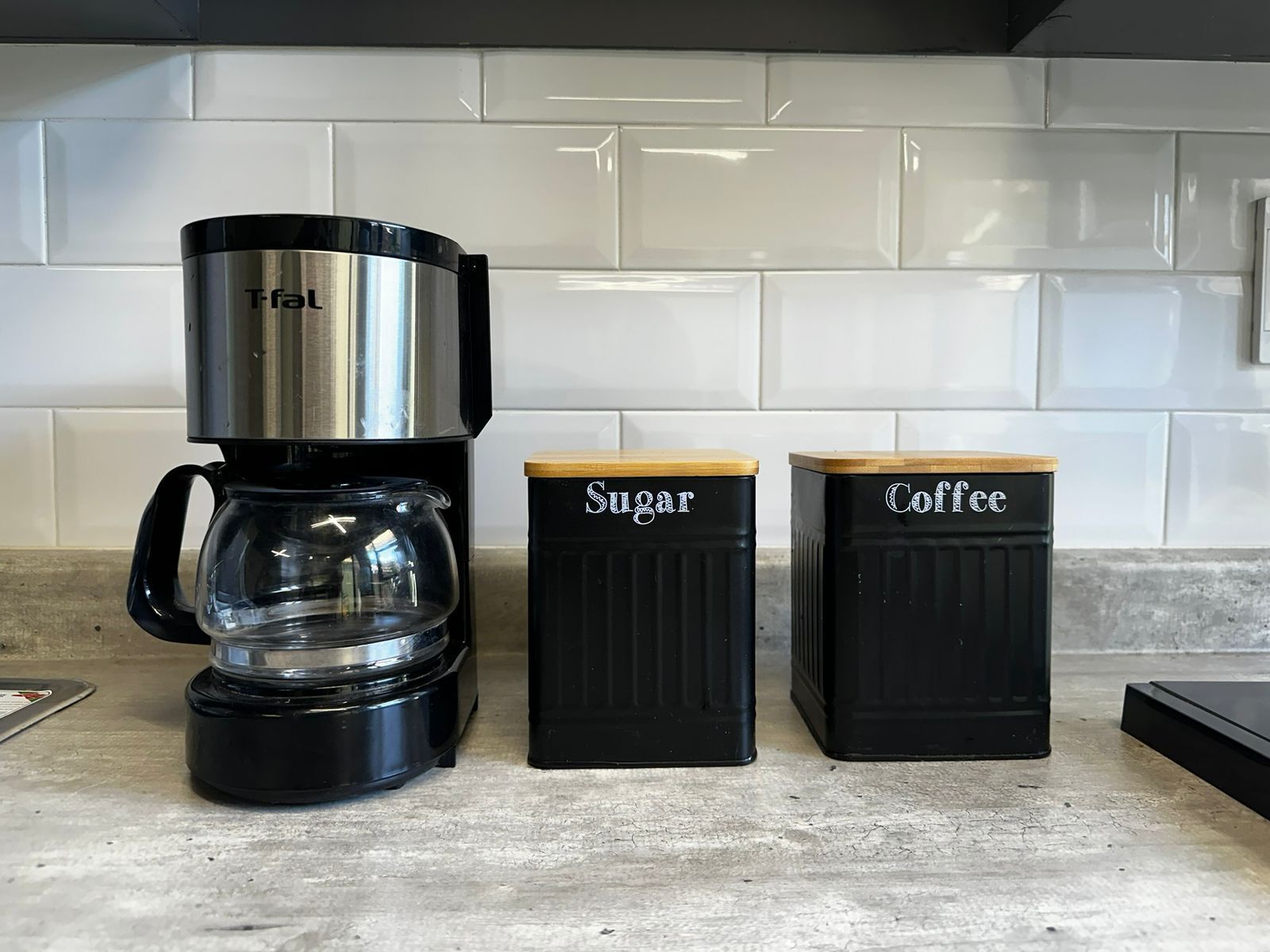 A coffee maker, a sugar container, and a coffee container on a kitchen counter.