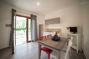 A modern kitchen with a dining area, a TV on a stand, and a sliding glass door to the outside.