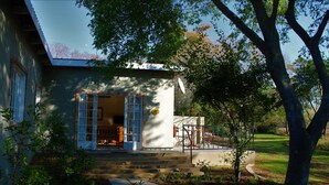 A house with a front porch, steps leading to the entrance, and a small garden area with a tree and shrubs. - Sweet Thorn Tree Spacious Cottage for 2 People With Great Terrace! (Muldersdrift)