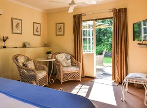 A room with a bed, two wicker chairs, a small table, and a television. - Rockfig Cottage for 2 People With Wonderful Private Terrace in Garden! (Muldersdrift)