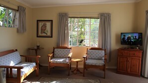 A living room with a sofa, two armchairs, a small table, a TV, and a window with curtains.