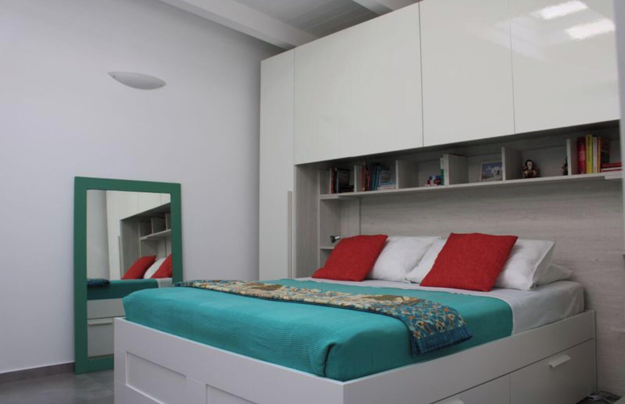 A bedroom with a bed, a mirror, and a built-in bookshelf.