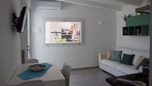 Ein modernes Wohnzimmer mit Essbereich, weißen Wänden, einem großen Fenster und einem grünen Regal.