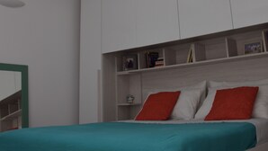 Ein Schlafzimmer mit Dachfenster, einem weißen Kleiderschrank und einem Bett mit türkisfarbenen Bettwäsche.