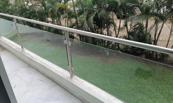 Un balcon doté d’une rambarde en métal, donnant sur un espace verdoyant planté de palmiers.