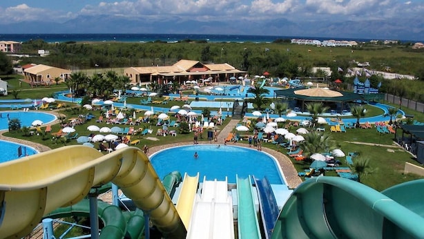 Un parque acuático con múltiples toboganes y piscinas, rodeado de edificios de resort y vistas al océano.