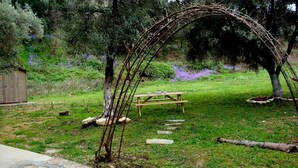 Un arco rústico de madera, una mesa de picnic y un sendero de piedra en un exuberante jardín.