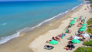 Una playa con filas de tumbonas y sombrillas, un mar azul cristalino y una orilla arenosa.