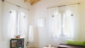 Una habitación con techo de madera, un sofá verde, una mesita, una lámpara de pie y una ventana con cortinas.
