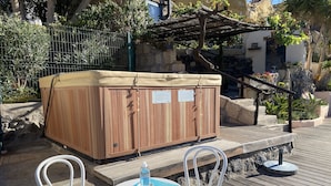 Een houten jacuzzi met een beige deksel, twee witte stoelen en een tafel met een blauwe onderzetter.