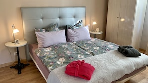 Een netjes opgemaakt bed met bloemenbedrukking, twee nachtkastjes met lampen, een kledingkast, en een rode handdoek op het bed.