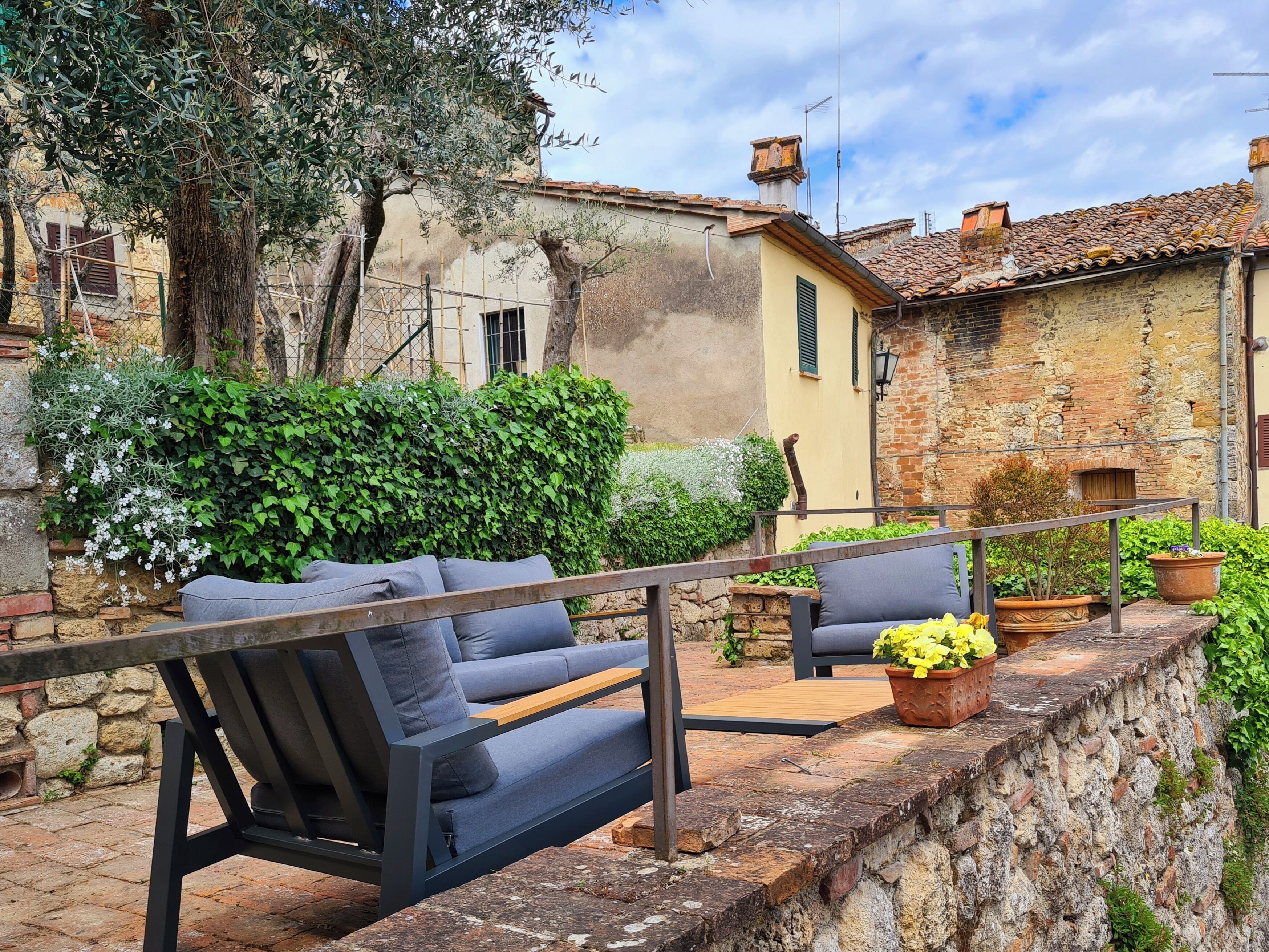 A courtyard with a sofa and chairs, surrounded by stone walls and greenery.