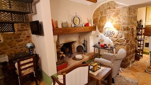 Un salon rustique avec des murs en pierres apparentes, une cheminée, des meubles en bois et un téléviseur fixé au mur.