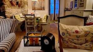 Un salon confortable avec un canapé, un fauteuil, une table et un lit. On y trouve une cheminée, une horloge et un tableau accroché au mur.