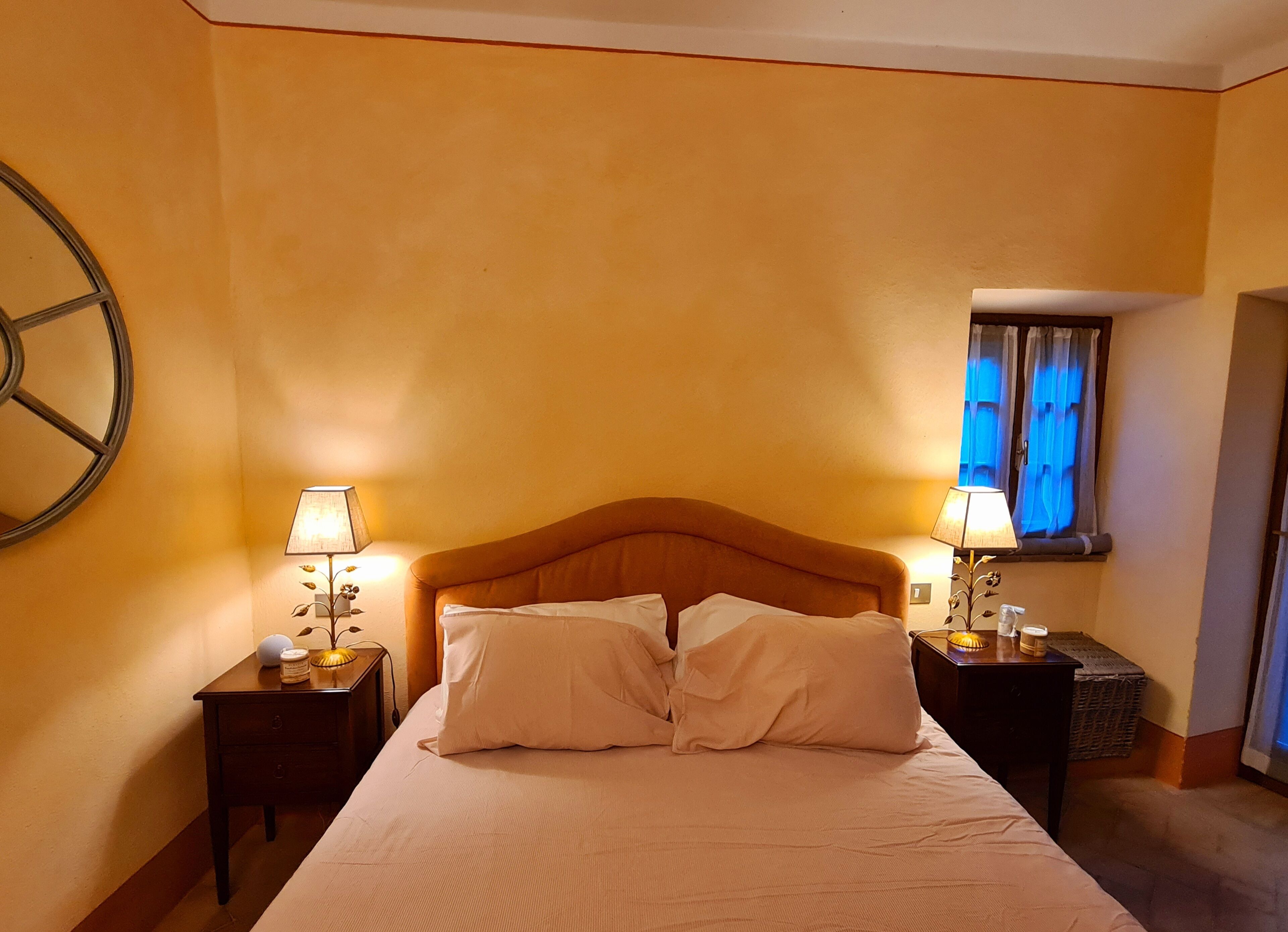 A hotel room with a bed, two bedside tables with lamps, a large wall clock, and a window with curtains.