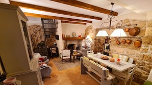 Une cuisine rustique avec un mur en pierre, des poutres en bois, une table à manger avec des chaises et un escalier en colimaçon.
