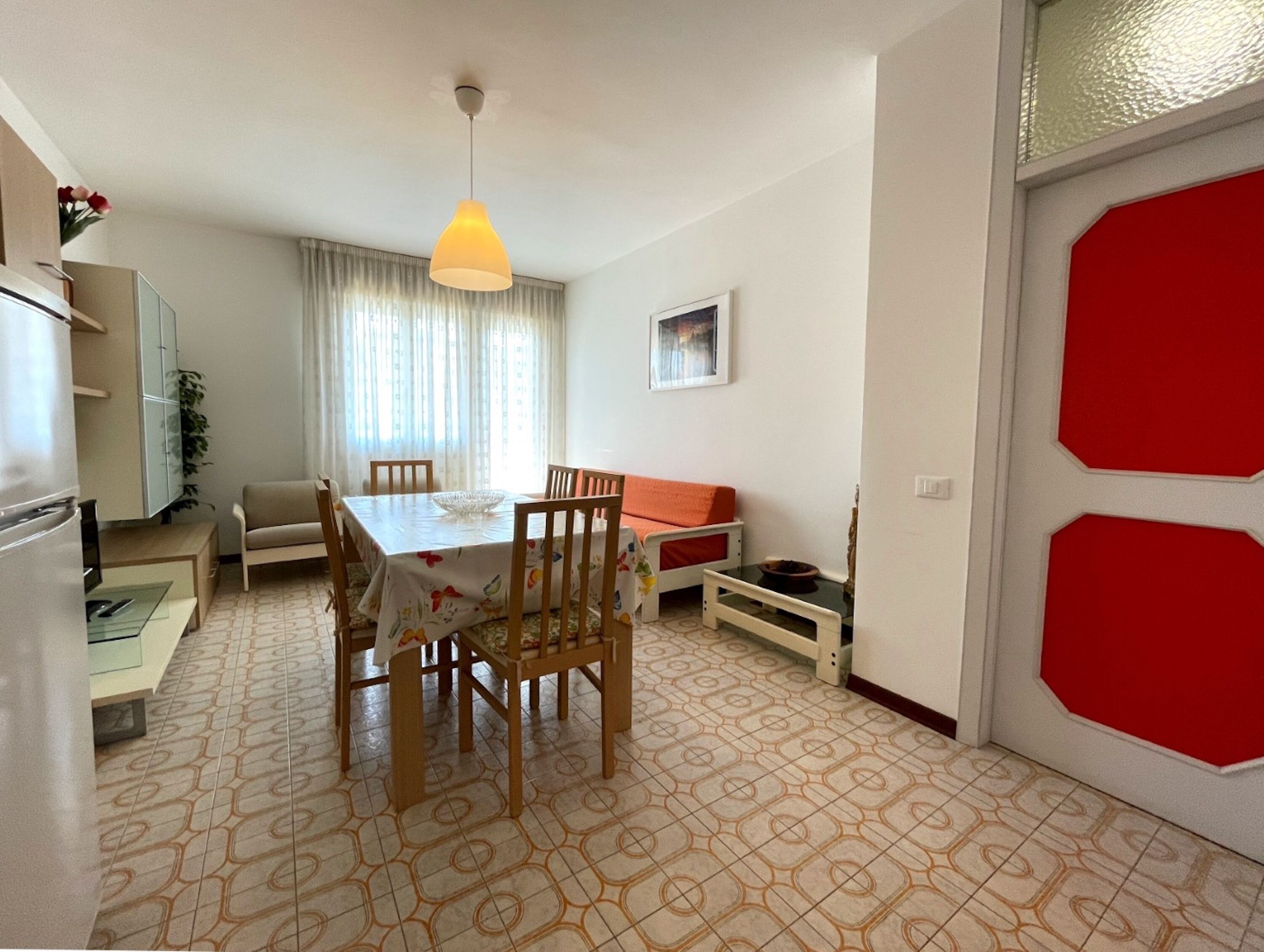 A dining area with a table, chairs, a sofa, and a red door.