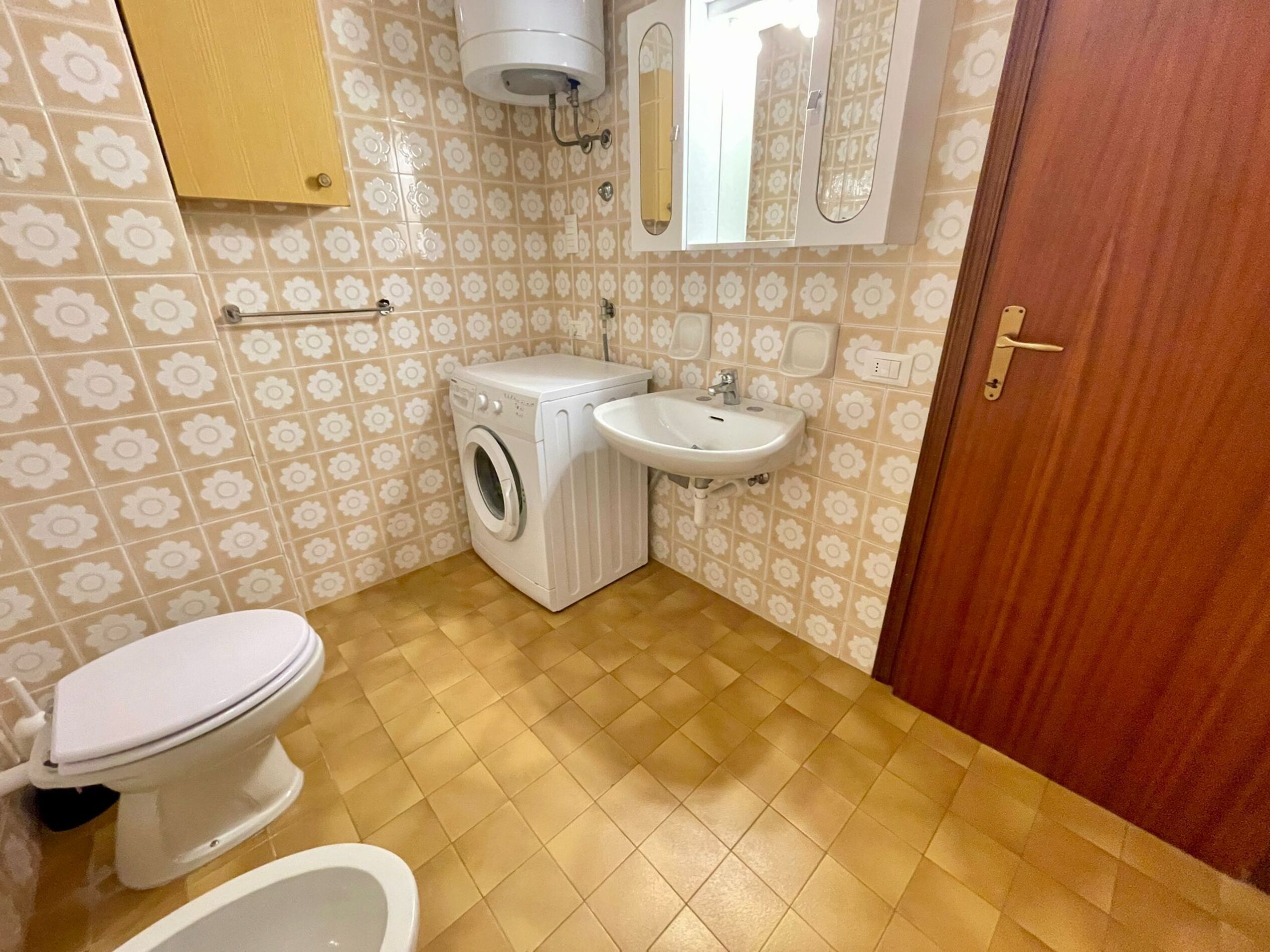 Une salle de bain équipée de toilettes, d’un lave-linge, d’un lavabo et d’une porte en bois.