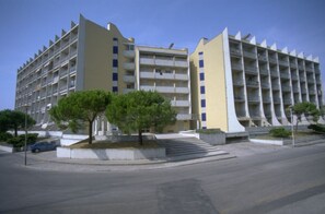 A multi-story building with balconies, a parking area, and trees.