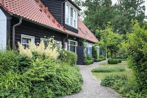 Une maison avec un toit recouvert de tuiles rouges, un chemin de gravier et une végétation luxuriante.