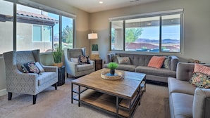 A spacious living room with a large window, a sofa, two armchairs, and a coffee table.