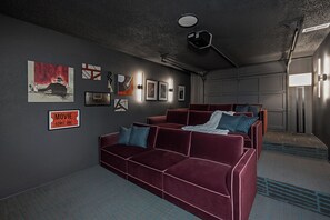 Une pièce avec un canapé en velours rouge, un panneau indiquant le prix des billets de cinéma, des photos encadrées et une porte de garage.