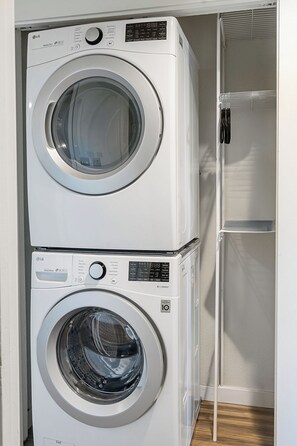 A stacked washer and dryer unit in a laundry room with a metal rack and a wooden floor. - Lake Views - Game Room/Movie Room - Seattle (Seattle)