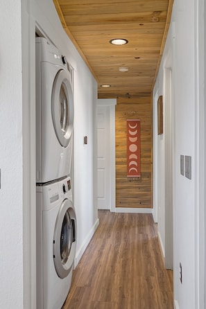 A laundry room with a washing machine and dryer, wooden flooring, and a wooden ceiling with recessed lighting.