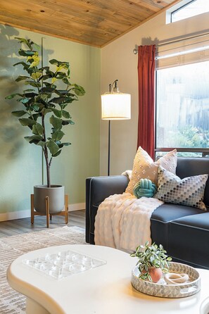 Un salon comprenant un canapé, une table basse, une plante en pot, un lampadaire et une fenêtre avec des rideaux.