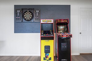 Dos máquinas de videojuegos, una de Pac-Man y otra de Mortal Kombat, frente a una pared con un dardo.