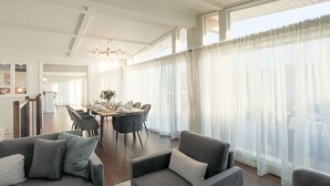 Ein geräumiger Wohnbereich mit Esstisch, zwei Sofas und transparenten Vorhängen.