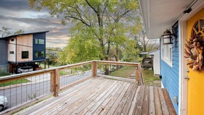 A wooden deck with a metal railing, a yellow door with a wreath, and a blue house in the background.