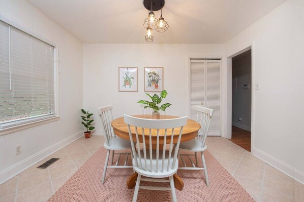 A dining area with a round wooden table, white chairs, a red patterned rug, and a ceiling light fixture.