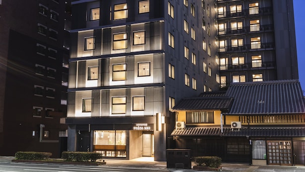 A modern multi-story hotel with illuminated windows, a crosswalk in front, and traditional architectural elements.