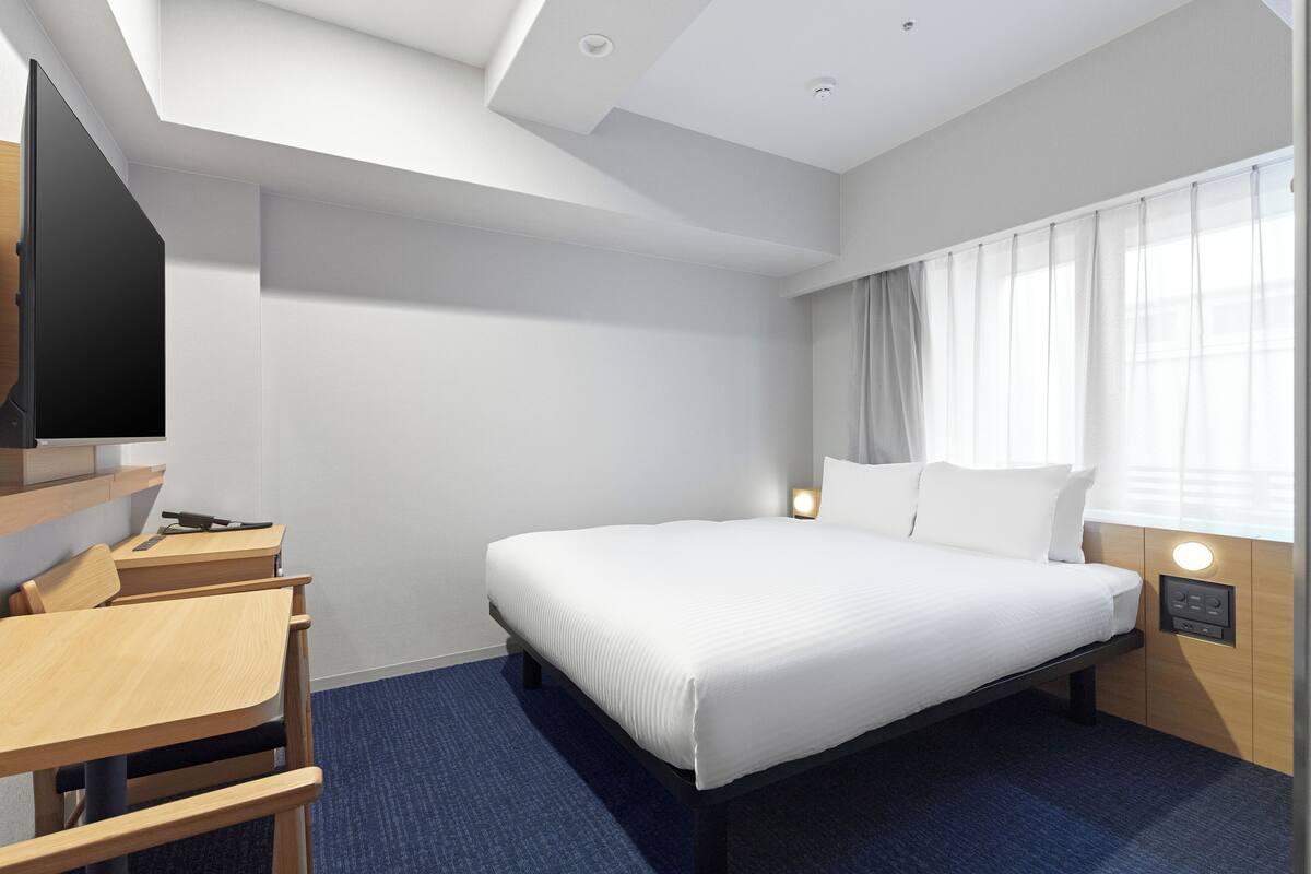 A hotel room with a bed, bedside tables, a desk, and a TV.