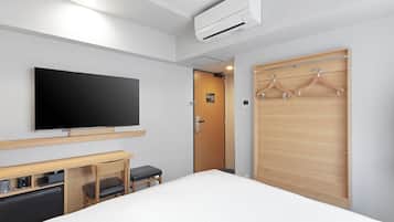 Ein Hotelzimmer mit Bett, Schreibtisch mit Stuhl, Fernseher, Kleiderschrank mit Kleiderhaken und einer Klimaanlage.
