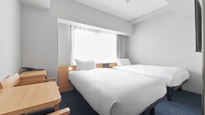 A hotel room with two beds, a desk, and a window with curtains.