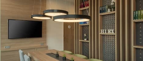 Une salle de conférence moderne, dotée d’une longue table, de chaises vertes et d’un téléviseur à écran plat fixé au mur.