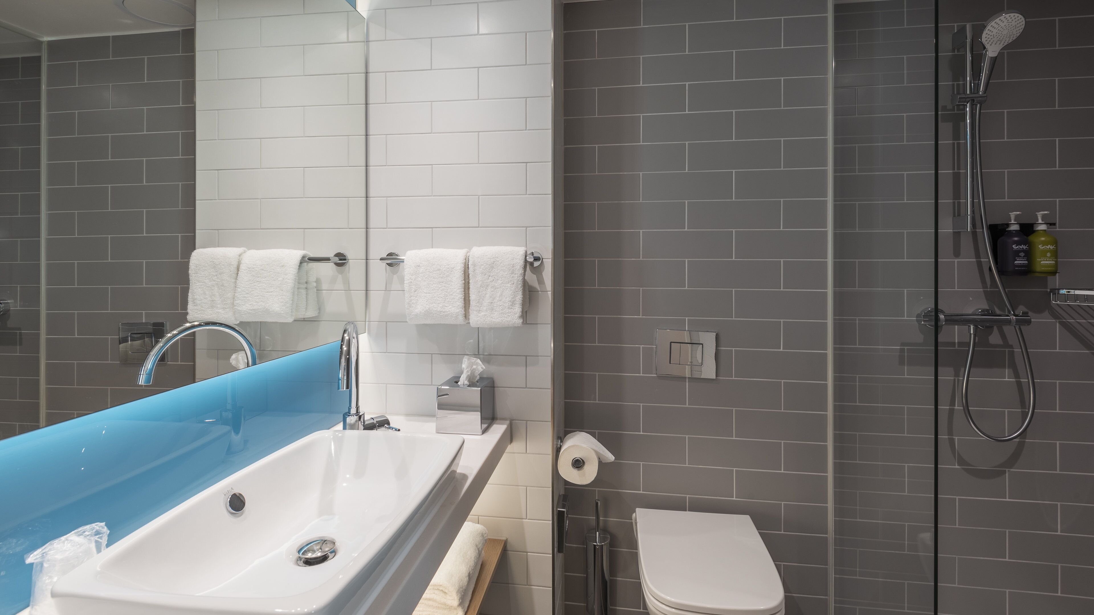 A bathroom with a blue vanity sink, white toilet, and a shower area.