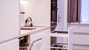 Une cuisine moderne avec des meubles blancs, une bouilloire posée sur le plan de travail et une fenêtre avec des rideaux.